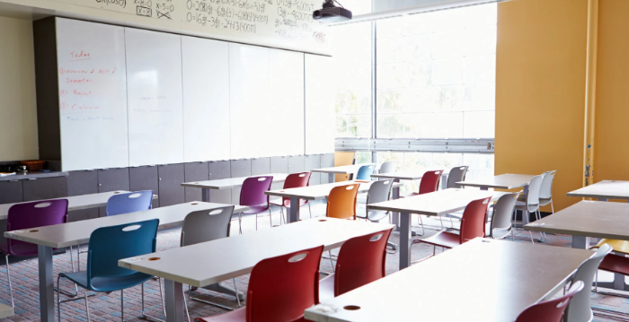 Picture of a classroom with tables and chairs facing a large whiteboard and a window as the side